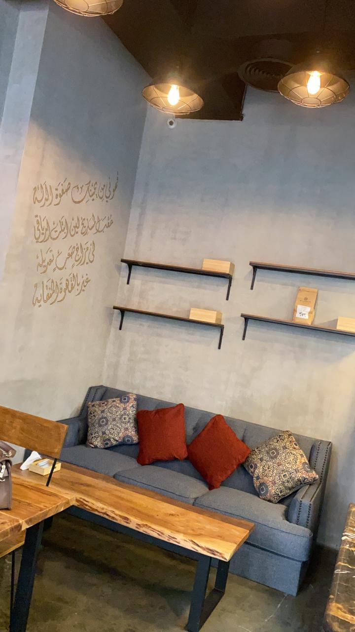 Cozy café seating with grey sofa, wooden tables, and wall shelves – ARC Design Dubai